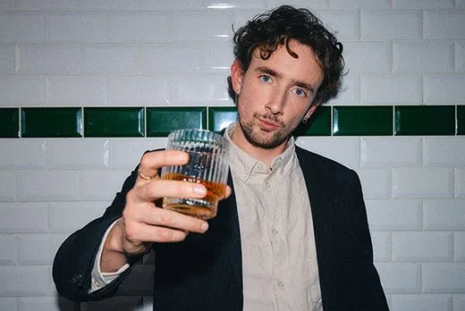 Young male saying cheers with a glass of whiskey