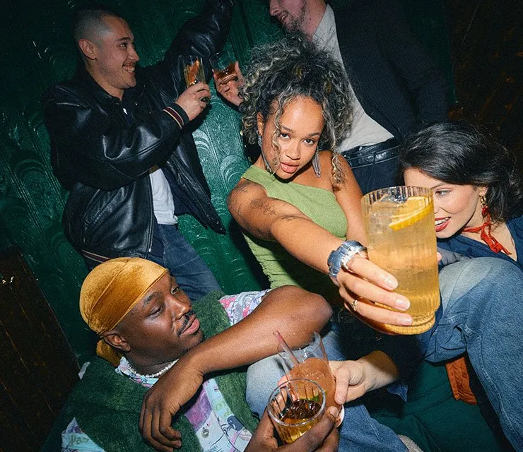 Group of young friends saying cheers with glasses of whiskey and mixers